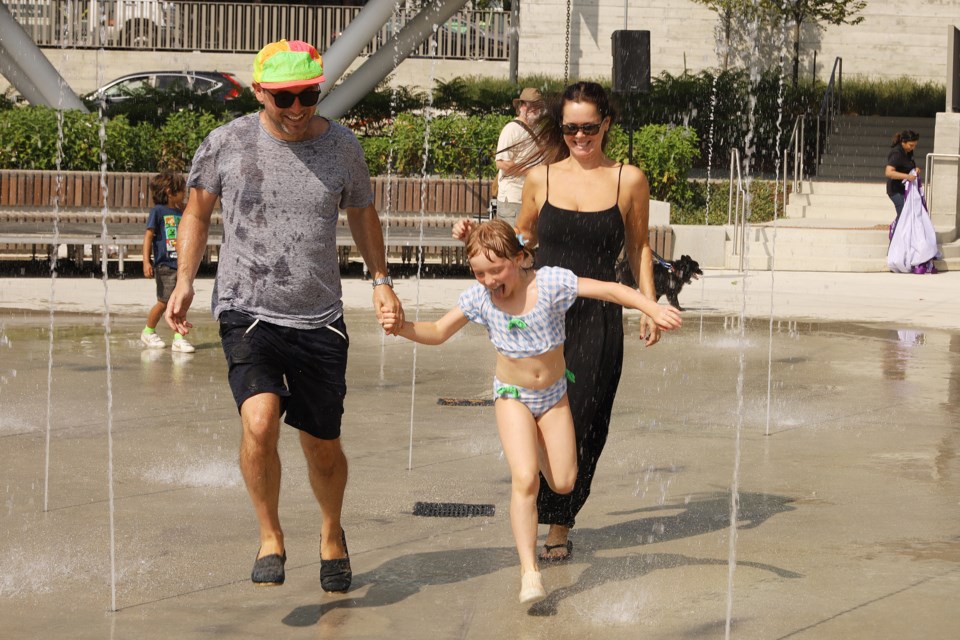 Aurora Town Square architect Thomas Nemeskeri, wife HeatherWoolvett and daughter Anna run through the water feature at the grand opening event Sept. 21.