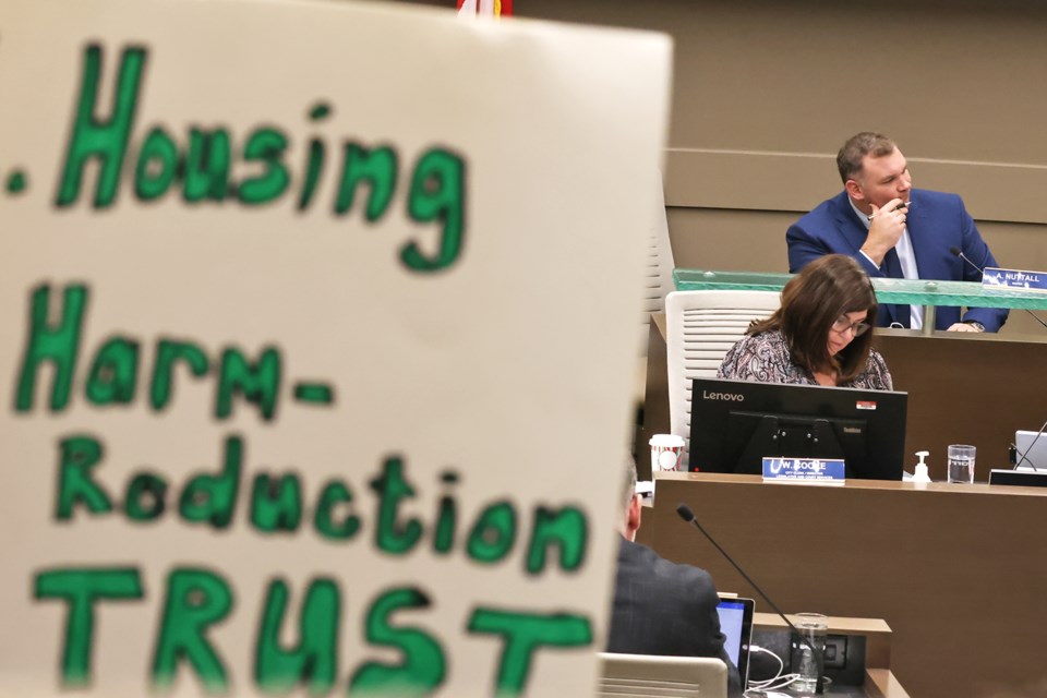 Mayor Alex Nuttall is shown as protesters hold signs during the Barrie city council meeting on Nov. 13, 2024.