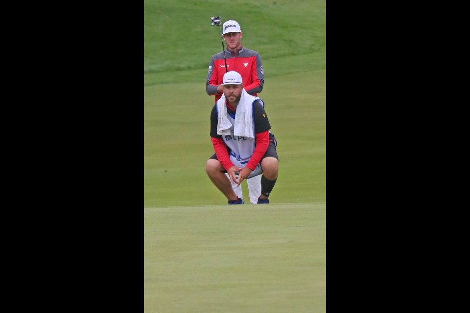 Caddie Mitchell Theoret crouches and surveys the green as Taylor Pendrith looks on at the RBC Canadian Open in 2023.