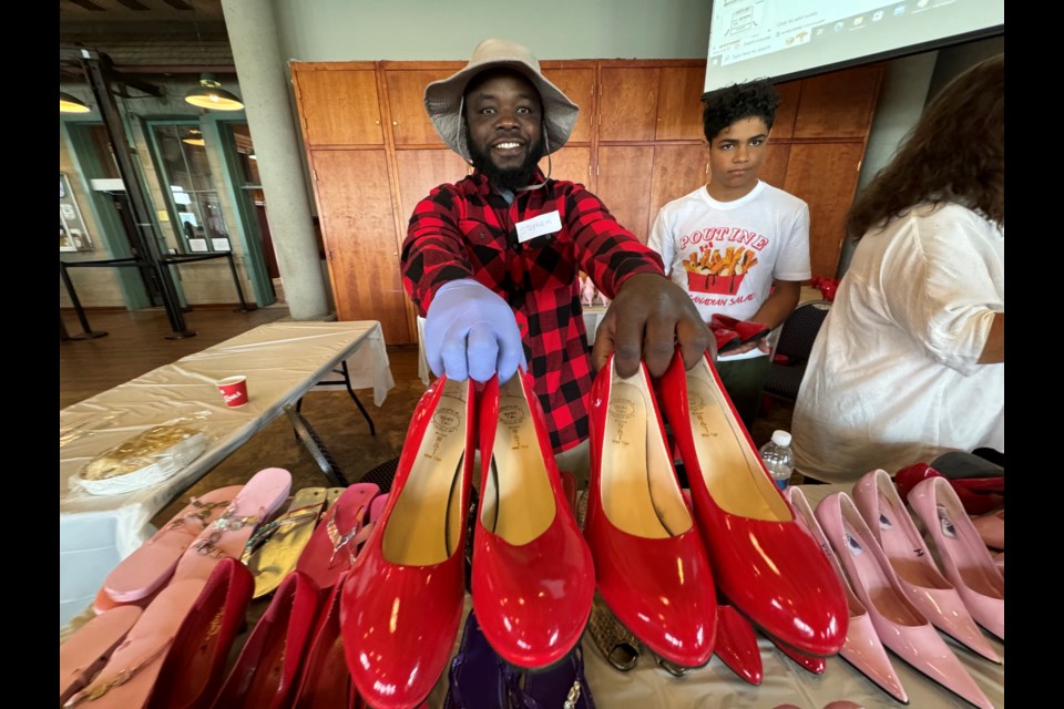 Volunteer Stephen Mwape helps participants find the right fit of heels for the 15th annual Walk a Mile in Her Shoes event Saturday.
