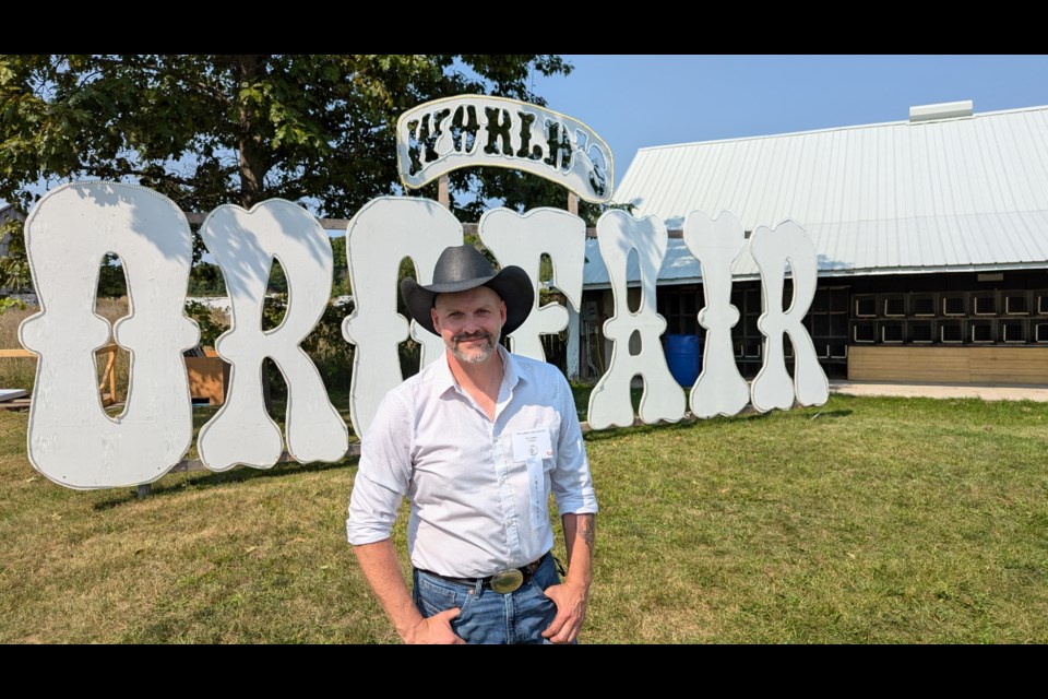 Ed Campbell, president of the Oro World's Fair, poses in front of the fair's sign — a popular selfie location for visitors.