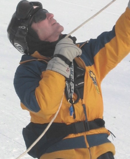 A rescue team member holds a rope tight before a stranded skier comes down it on a pulley.