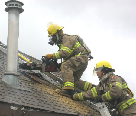 A fire fighter uses a chain saw on the roof at 781 Worthington St. W to cut a hole for a fire hose. Photo by Phil Novak.