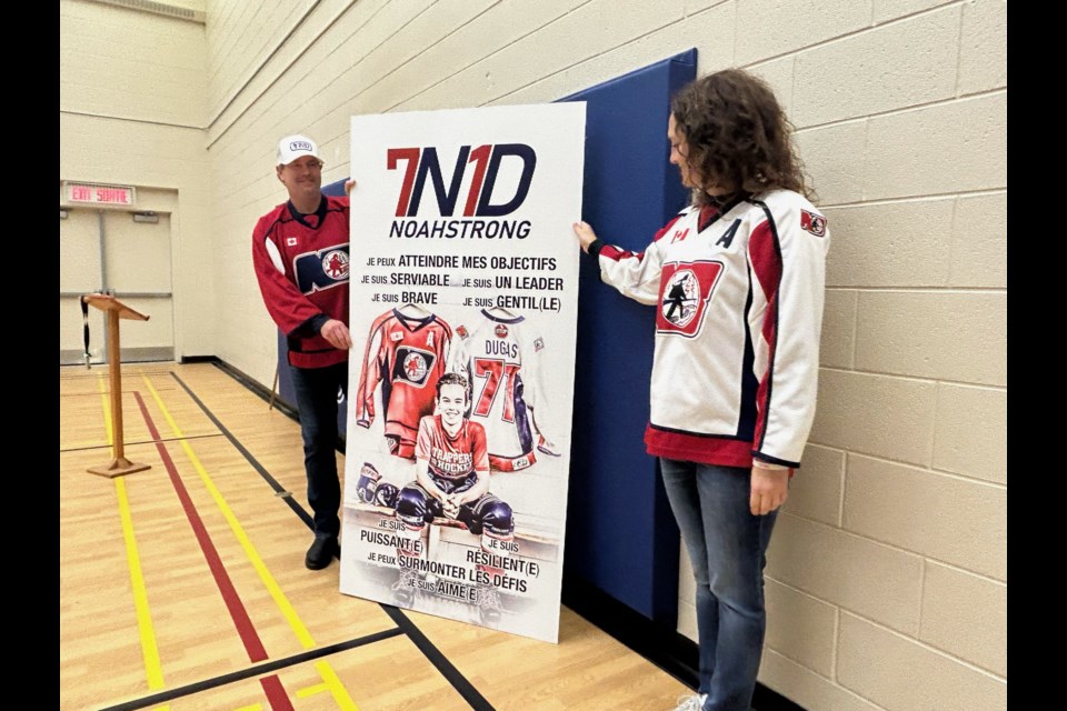 Dave and Jody Dugas stand next to the Noah Dugas sign that will be put up in the Saint-Raymond elementary school gymnasium. 