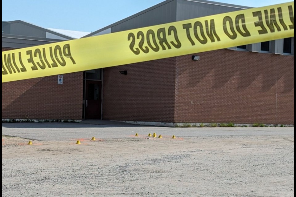 Police tape shows the shooting scene at Holy Cross school. Evidence identification markers can be seen on the asphalt.