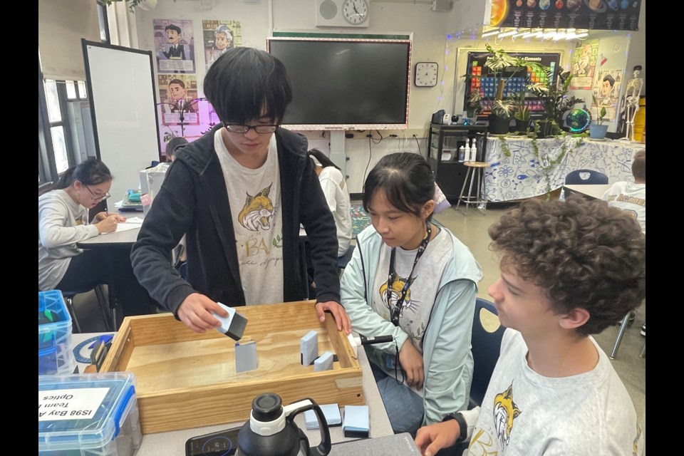 Three members of I.S. 98 Bay Academy's Science Olympic team work on their device for the Olympiad's optics event.
