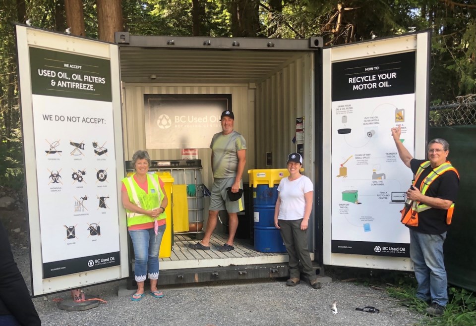 Four people standing in front of a shipping container that's the new oil facility