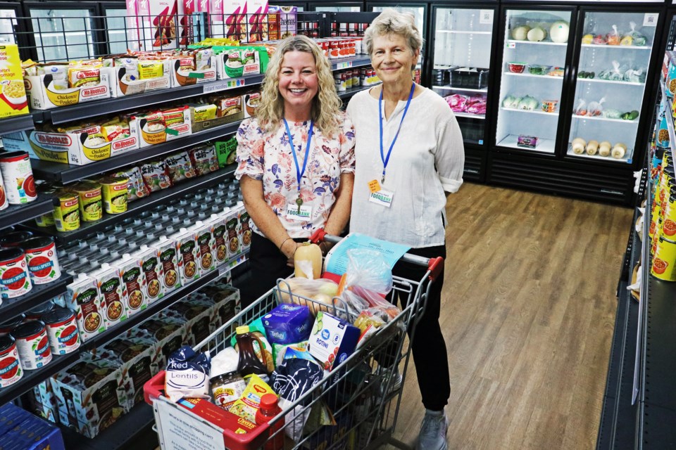 From left: Helping Hand Food Bank Executive Director Carolyn Khan along with staff member Grace Wittig filled a shopping cart to illustrate the amount of food a family can get from the food bank each month, during their open house on Sept. 22, 2024.