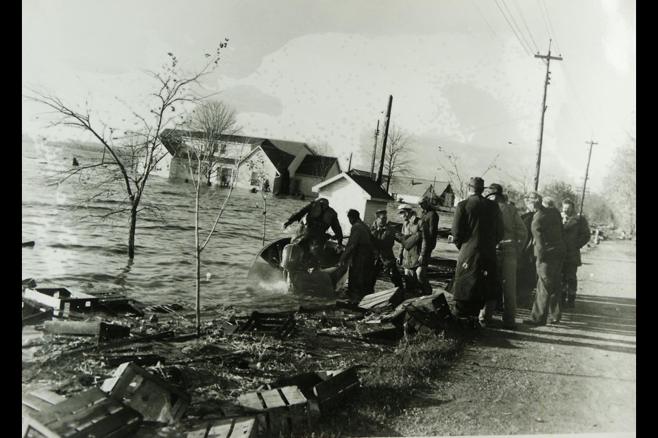 The landing place for boats on the dyke near Peter Verkaik's house (in the background) during Hurricane Hazel in October 1954. A boat delivers some marsh folks to dry land. In this picture, the person on the far right is Leon Radder, Auke Ellens wears the captain's cap, and the person standing behind him is Albert Van Dyke.