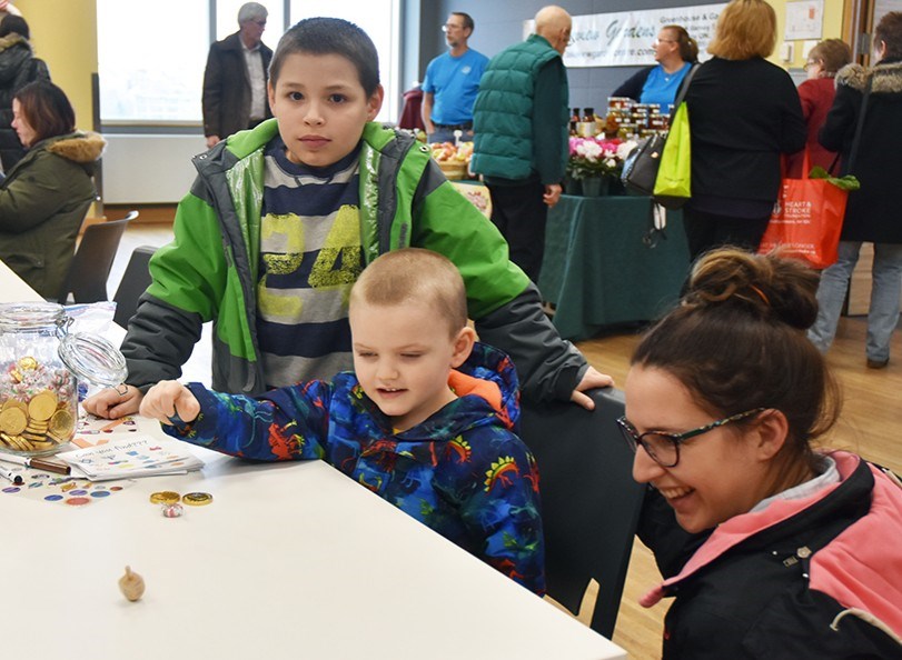 Brody, 10, Ronald, three, and mom Erin learn how to play the dreidel game, at the Bradford Farmers’ Market, Dec. 1. Miriam King/BradfordToday