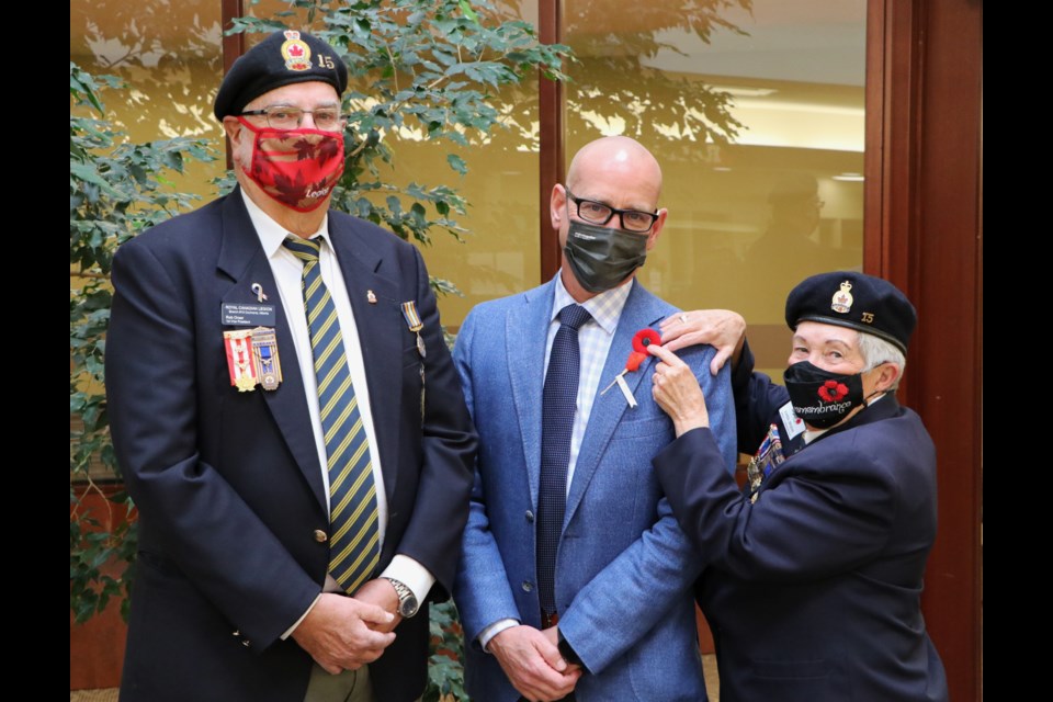 Royal Canadian Legion members Rob Orser and Karen Bruens pin both the traditional poppy and a poppy reminiscent of the first poppies distributed in Canada after the First World War, on mayor Jeff Genung at the Cochrane RancheHouse Oct. 28, to kickstart the 100th anniversary of the Remembrance Day poppy campaign. (Jessica Lee/The Cochrane Eagle) 