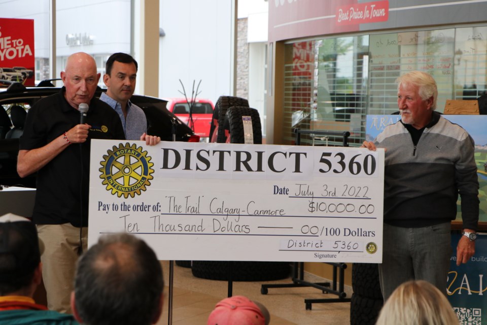 District governor of Rotary International District 5360, Martin Parnell, presents a check to Cochrane to Calgary Trail Steering Committee member Dan Kroffat in support of the Bike-A-Thon and trail project at Cochrane Toyota July 3. The $10,000 donation will be matched by the provincial government, according to Parnell. (Jessica Lee/The Cochrane Eagle)