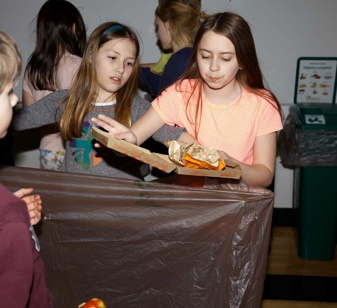 Daelyn Lyttle, left, Teagan Wattand help students sort various garbage into its proper waste baskets after lunch at Holy Spirit&#8217;s Elementary in Cochrane on Friday,