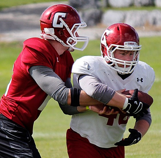 Cobras senior quarterback Cody Stevens hands-off to fullback/linebacker Mac Chaisson at Cochrane High School&#8217;s first day of football training camp Aug. 24. Forty-five