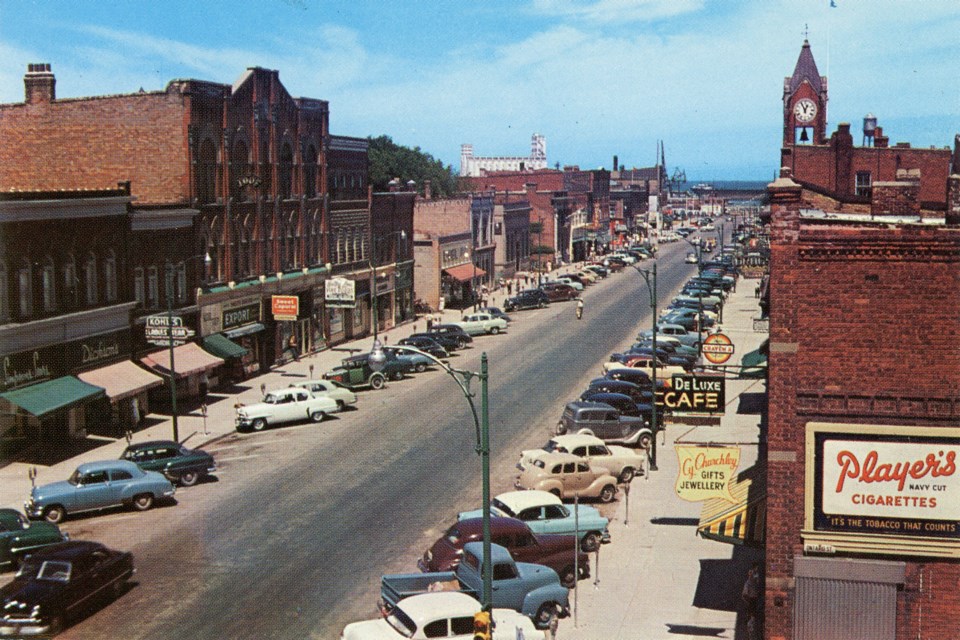 Colour postcard of Collingwood’s main street, showing Cy Churchley’s hanging business sign to the left of the Player’s Cigarettes advertisement. The yellow sign was donated to the Collingwood Museum’s collection in 2004. 