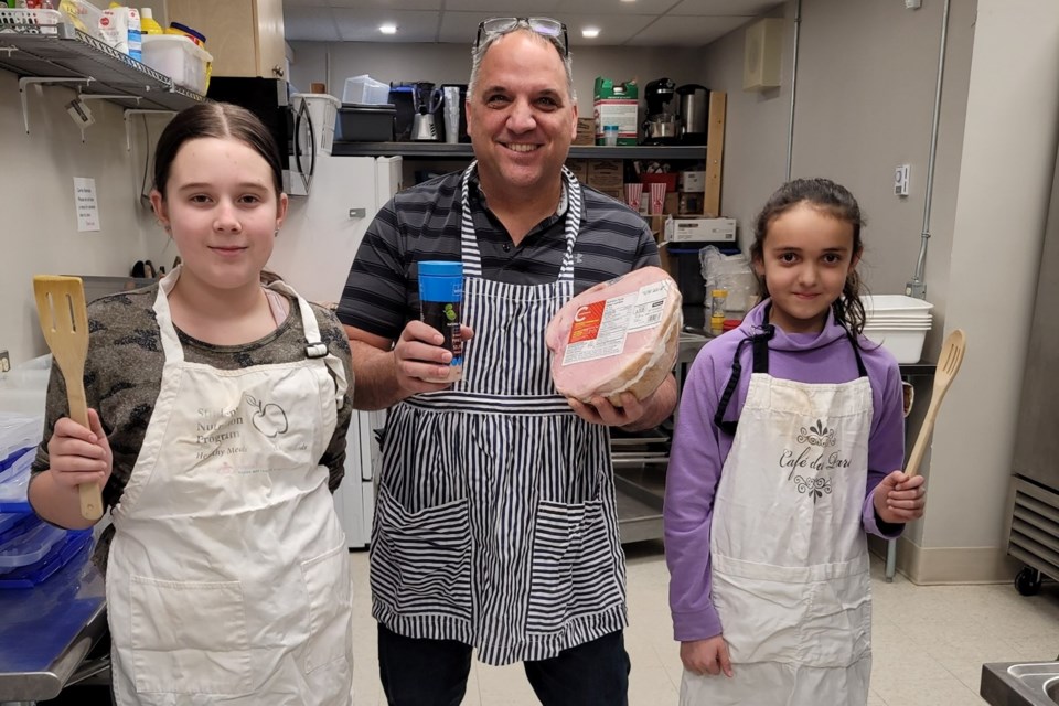 Students Peyton Flood (left) and Iris St. Amand assist principal Angelo D'Amato (centre) with cooking meals for other students