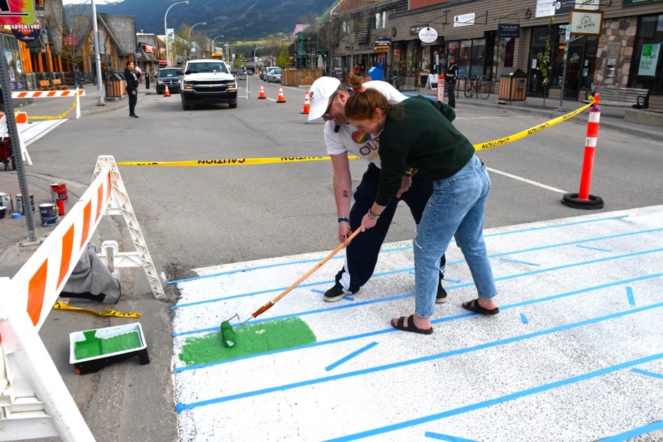 Mychol Ormandy, executive director of OUT Jasper, and volunteer Krista Gillese begin painting the rainbow crosswalk outside of TD Bank in Jasper on Thursday, May 30, 2024. | Peter Shokeir / Jasper Fitzhugh