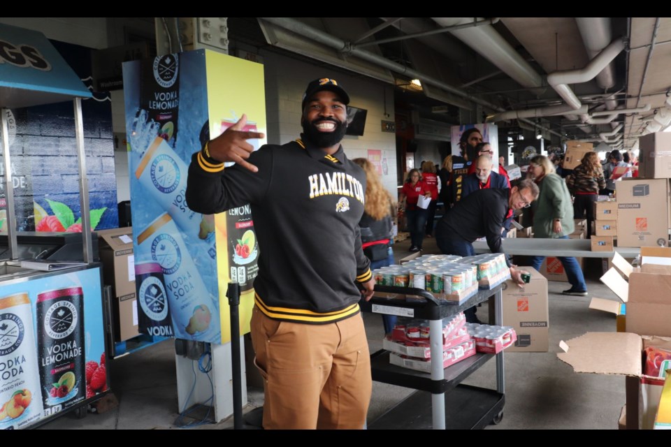 Former Hamilton Tiger-Cat Simoni Lawrence carries heavy flats of canned food for volunteers to pack. He put down the cans for this photo. 