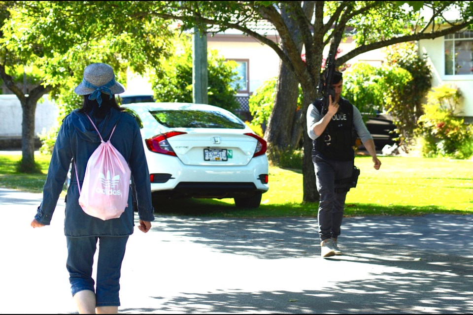 A young woman passes by a heavily-armed police officer on Jasmond Avenue following a police incident May 30 around 2-4 p.m. Graeme Wood photo