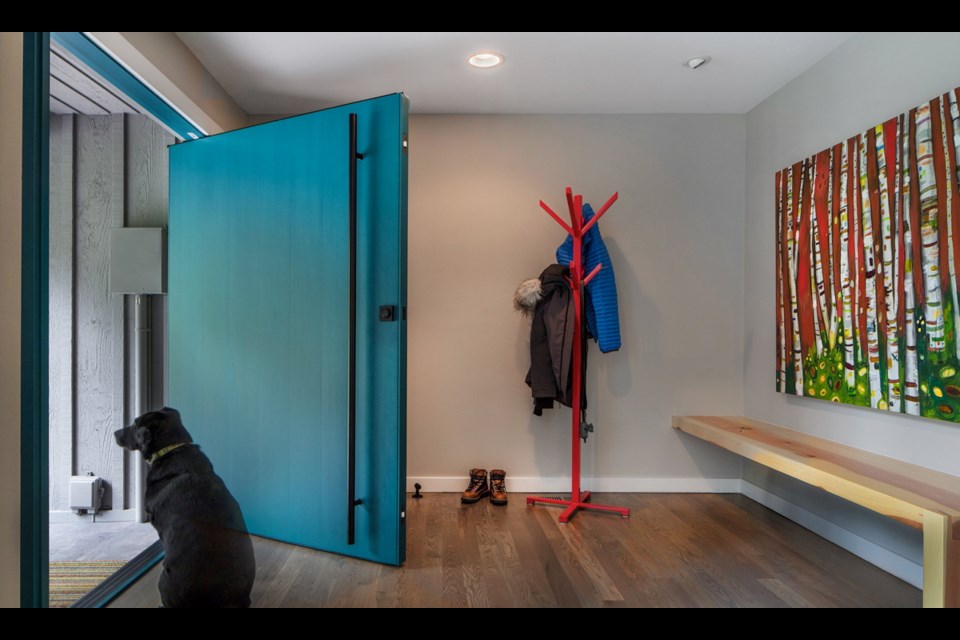 Finley, the dog, guards the new statement-piece pivot door in the reconfigured entry of Kelsey and Ross Henry's Woodinville, Washington, home. The built-in bench was crafted from a tree felled in a windstorm at Ross's family lake house in Idaho.