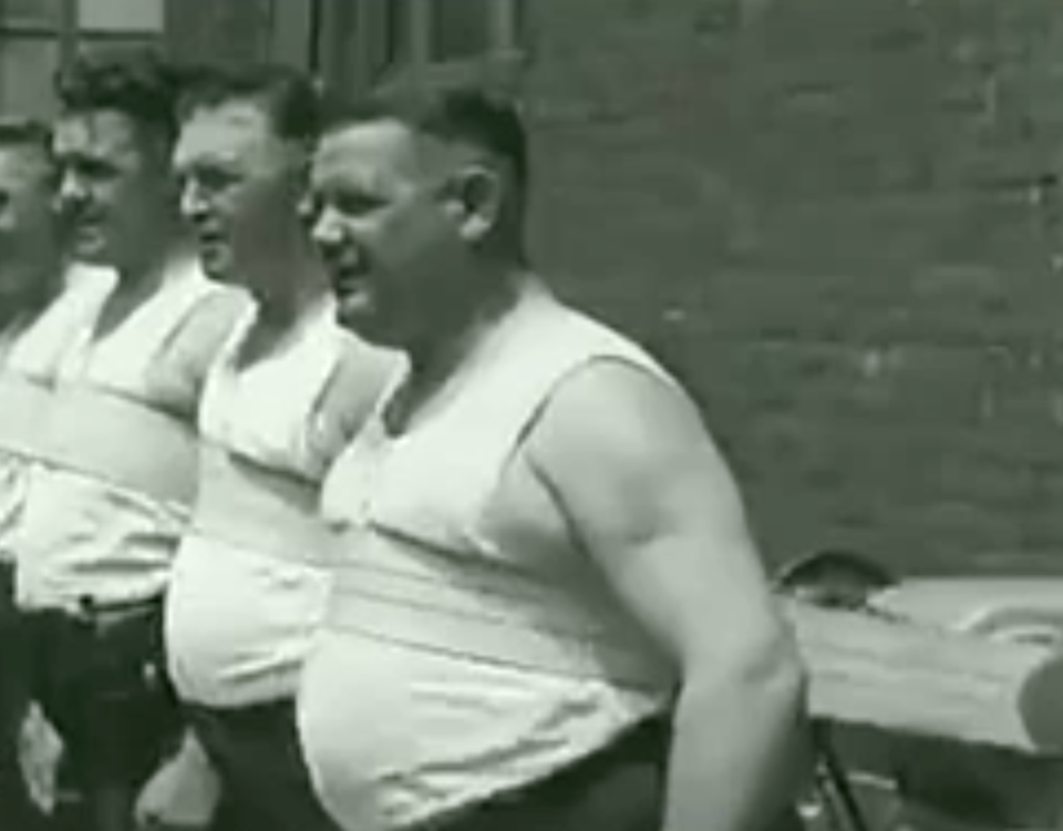 A group of men use the Mueller Belt in this screenshot taken from 1930s footage. The vibrating contr