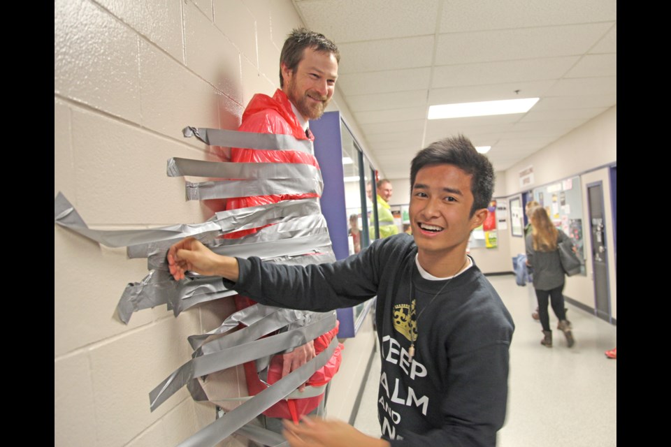 Tape time: New Westminster Secondary School student and event organizer Jethray Tecson duct-tapes principal Phil Cookson to a wall for the Doctors Without Borders fundraiser held at the school on Friday, Nov. 29.