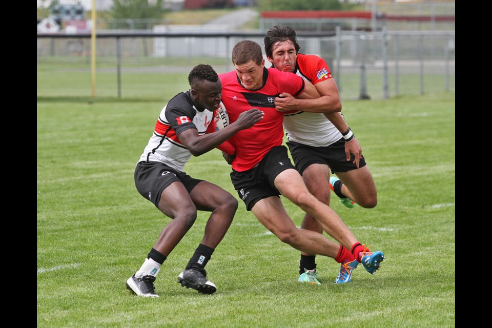 St. George’s Cathal Long grips the ball and surges forward against two Carson Graham tacklers in a senior boys AAA rugby championship quarterfinal at Abbotsford Exhibition Park on May 28, 2014.