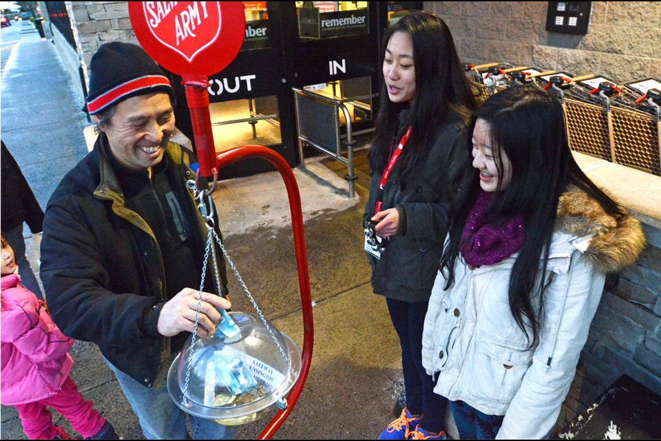 Burnaby North Secondary Small Steps volunteers Kethy Lin, middle, and Lilyan Jia exchange holiday greetings with Rick Jang as he stuffs a donation into a Salvation Army Christmas kettle at the Kensington Safeway last week.