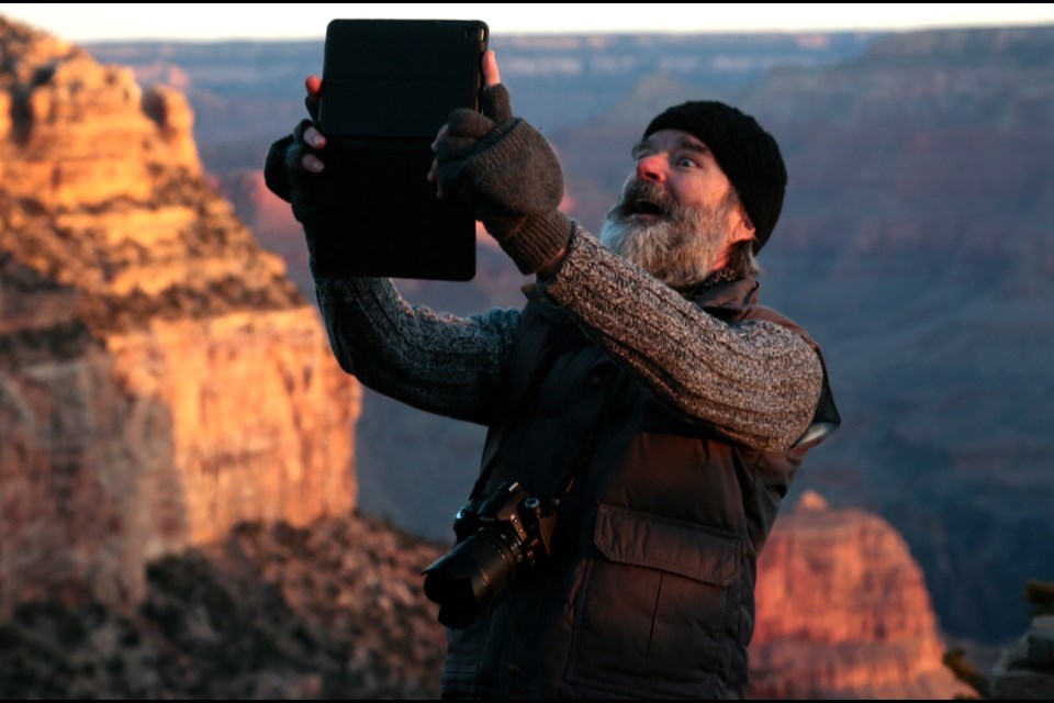 Artist Gregory Zeorlin holds his iPad in the air and smiles for a selfie along the South Rim.