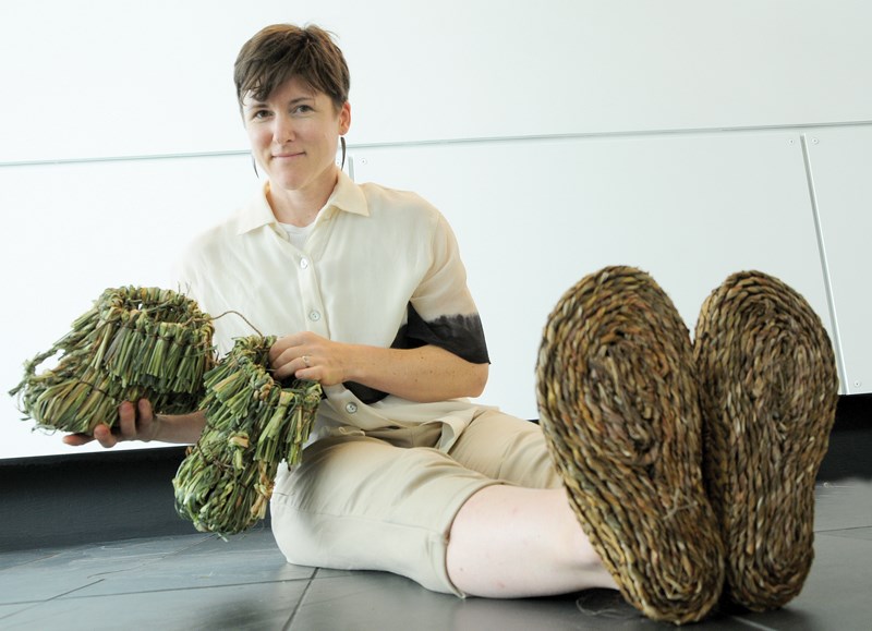 Artist and weaver Rebecca Graham wears a pair of shoes made from blackberry bark and New Zealand flax and holds boots made from reed canary grass. Her woven footwear is on display at the Walking on the Land exhibit at the City Atrium Gallery inside North Vancouver City Hall until Aug. 24.