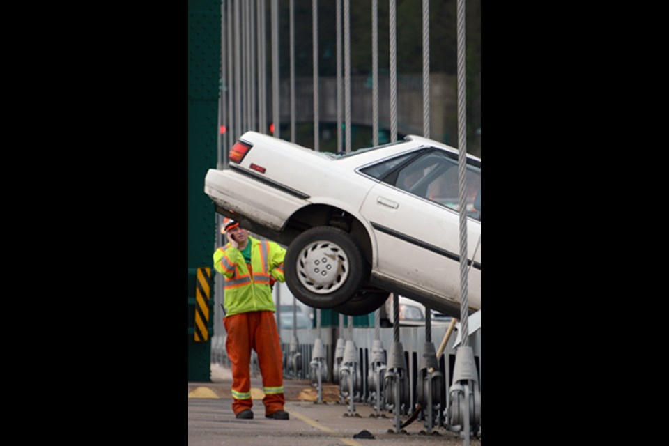 A member of the clean-up crew checks the rear of a car shunted almost onto the pedestrian walkway by the force of an accident on Lions Gate Bridge this morning.