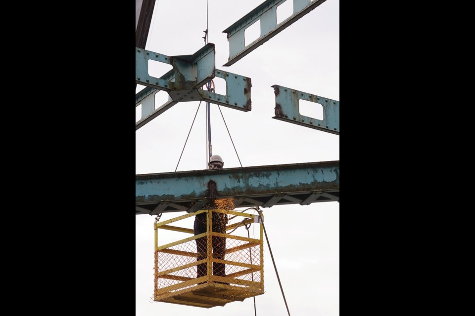 Chris Conn from B&B Contracting cuts apart the steel crossbars, dismantling the bridge structure for removal.