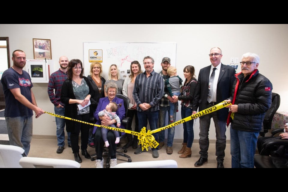 It was a family affair cutting the ribbon for Genco Asphalt Inc. From left are Cordell Fiest, Sebastian McClement, Jacqueline McClement, Krista McClement, Brie McClement, Hannah McClement, Doug McClement, Logan McClement (holding Roman), Laura McClement, Mayor Roy Ludwig and Councillor Dennis Moore. Sitting are Rosalia McClement (holding Eila). Photo by Brian Zinchuk