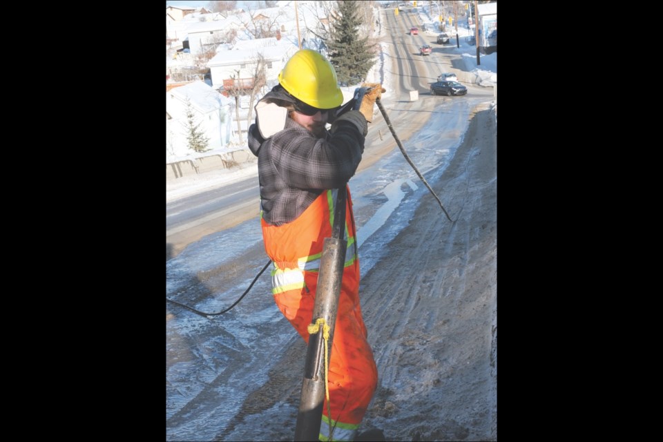 City of Flin Flon employee Tyler Whitbread inserts a hot-water-spewing tube into a frozen storm drain on Third Avenue on Wednesday afternoon. The frozen drain temporarily rerouted traffic around the hill.