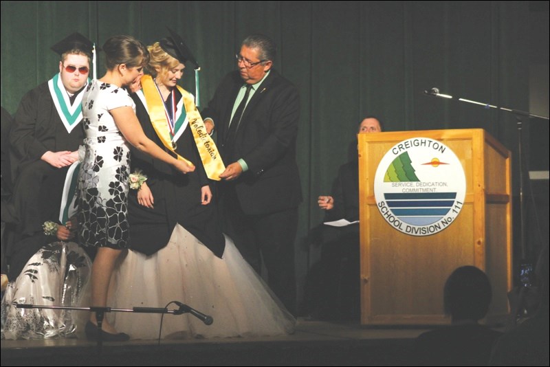 Taylor Kryschuk received the valedictorian sash from MLA Doyle Vermette with help from principal Stacy Lair during the graduation ceremony.