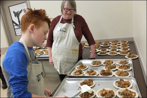 Volunteer Leland Feuerstein, 10, adds whipped cream to dessert for festivalgoers as fellow volunteer Maureen McBratney looks on.