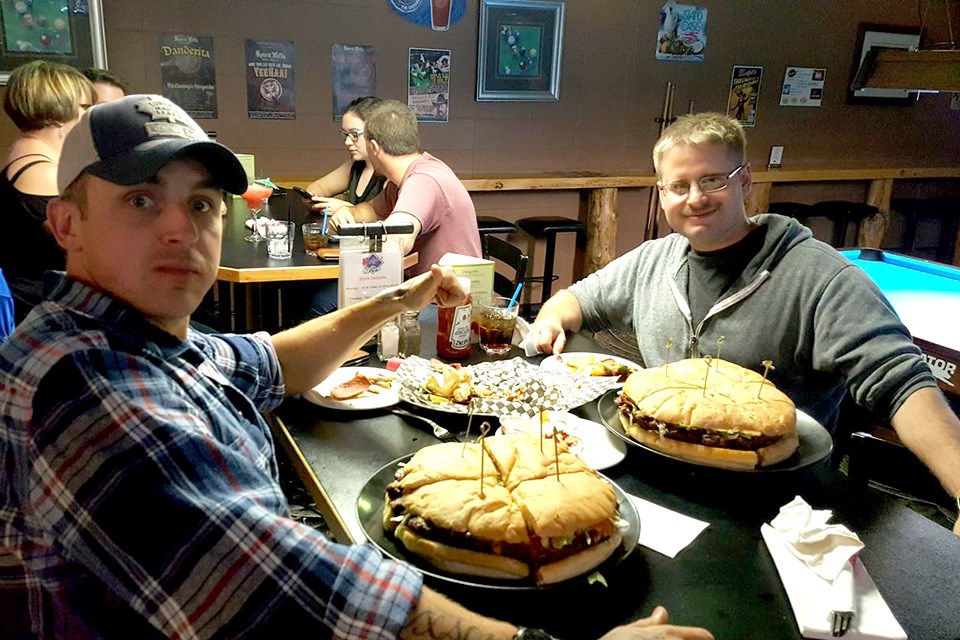 Two men sit at a pub table with huge burgers on their plates at Ralph's Texas Bar & Steak House in Medicine Hat. / Ralph's Texas Bar & Steak House | Facebook