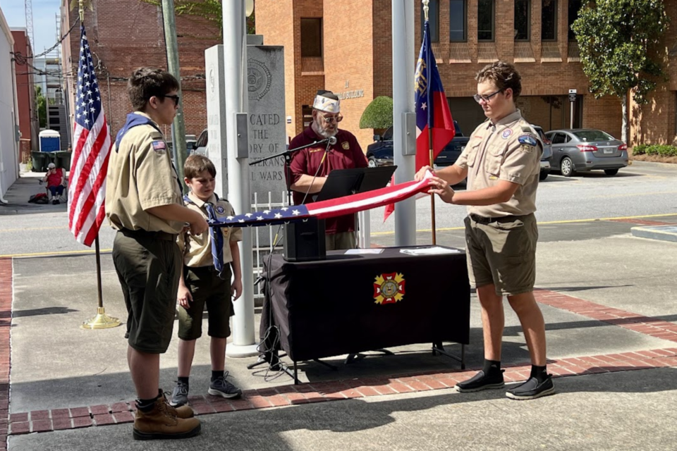 Boy Scout Troop 935 members John Hutflies (L), Waylon Brown (facing camera) and Evan Taormina fold the flag while VFW member Mike Cox speaks