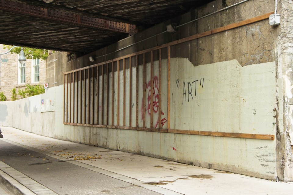 The space where the mural 'Cultivation' was installed sits empty with just mounts on the wall and the word 'art' spray painted with quotation marks. 