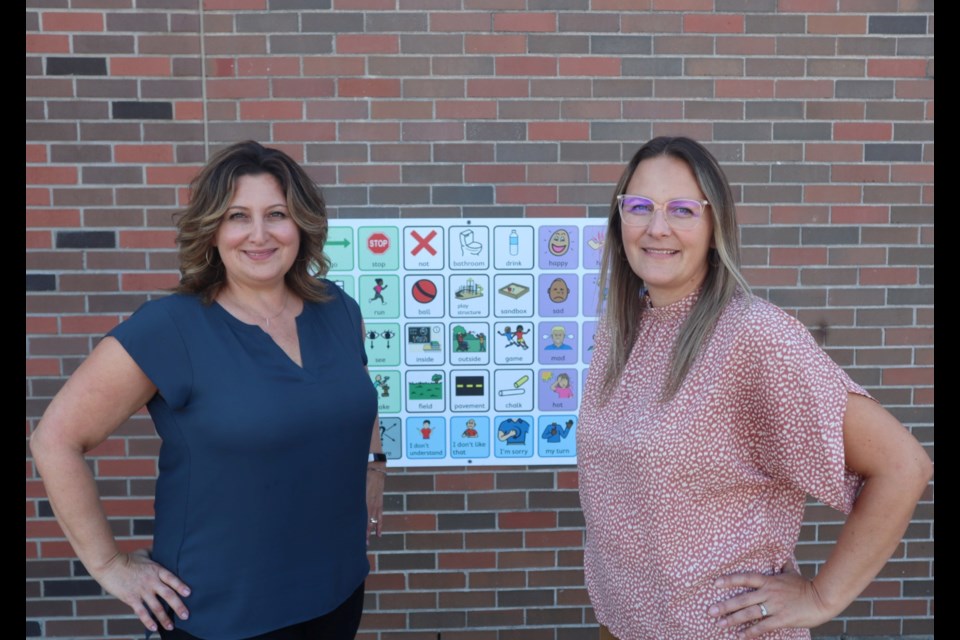 WCDSB speech-language pathologists Michelle Chimienti and Jessica Docker outside at St. Patrick Catholic Elementary School in front of one of its communication boards.