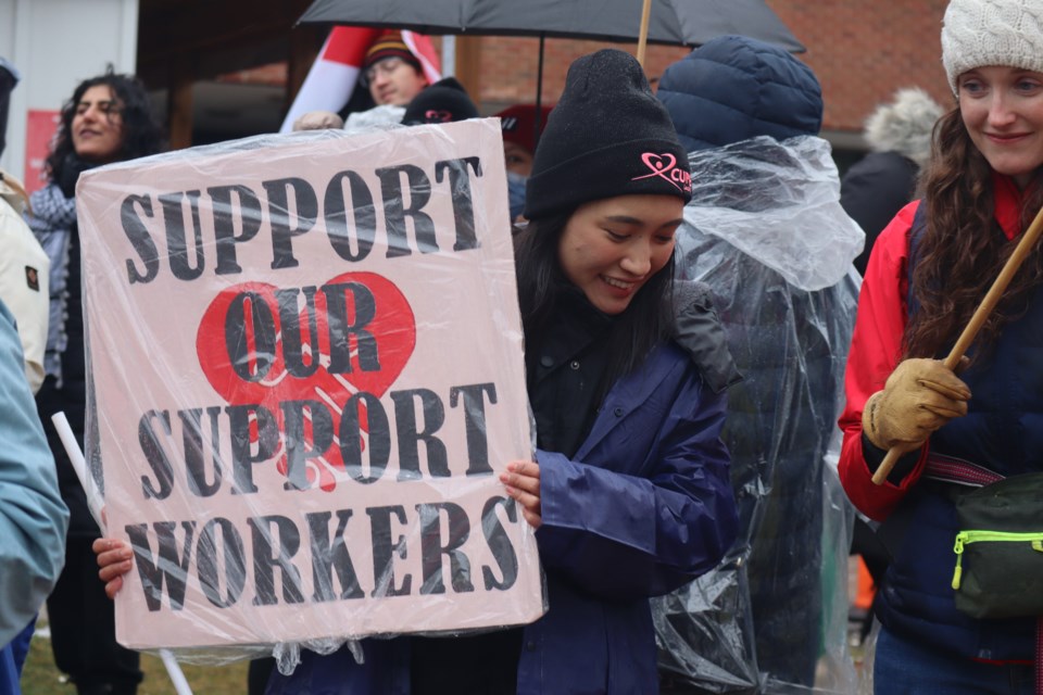 A rain poncho covered sign reads "support our support workers" at the rally supporting PSWs set to be laid off come May from the Guelph General Hospital.