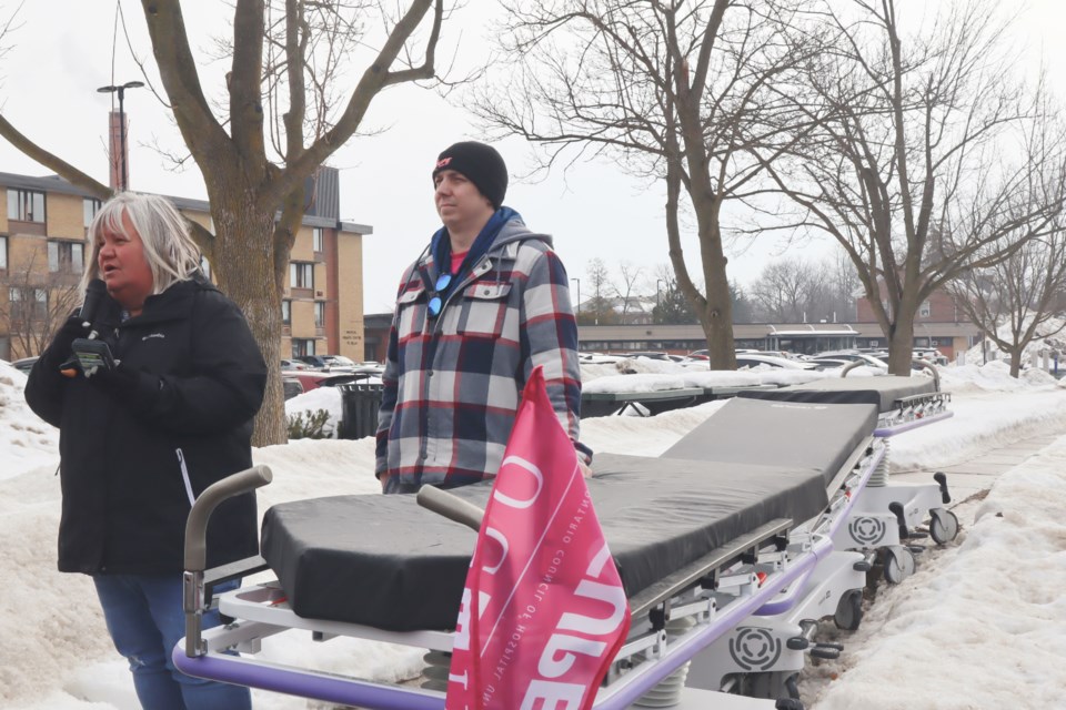 Sharon Richer, secretary treasurer of OCHU and Mark Zinger, vice-president of CUPE Local 57 beside a line of hospital beds on the sidewalk near Guelph General Hospital.