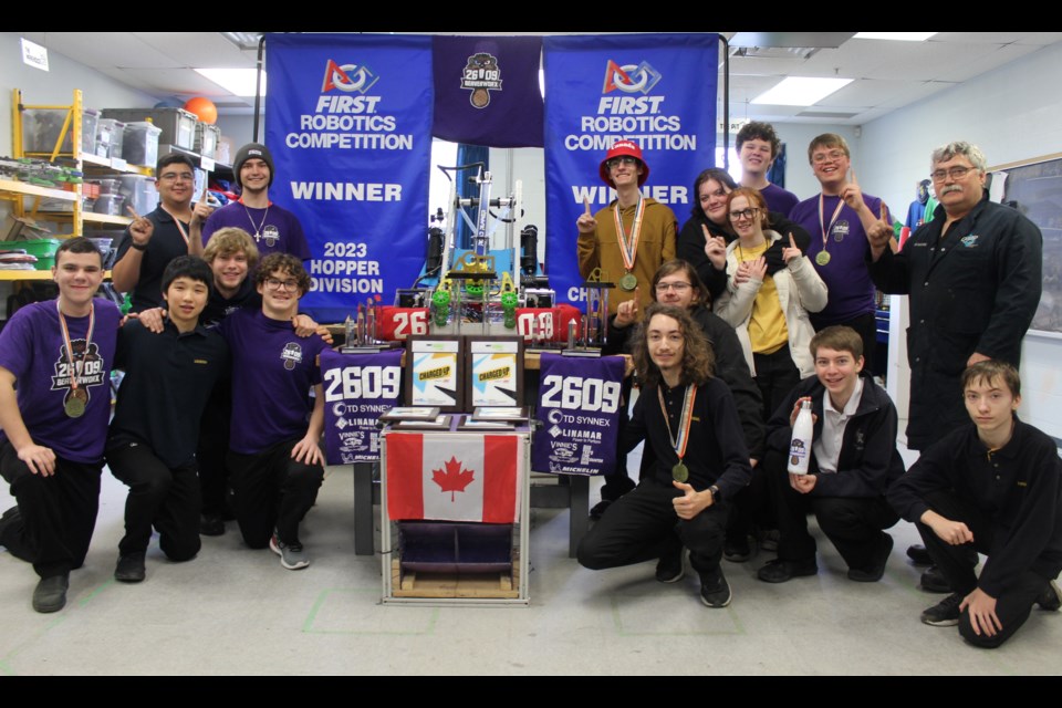 Members of Team 2609 BeaverworX at Our Lady of Lourdes Catholic High School huddles around their robot and collection of awards.