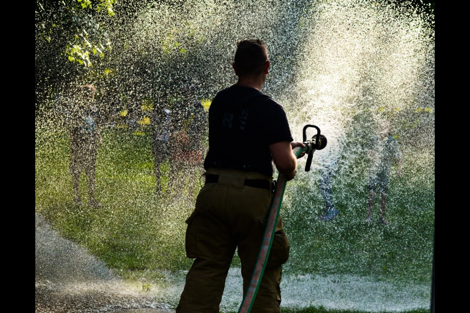 A Guelph firefighter launches water at waiting children at Hot Summer Nights at Norm Jary Park Thursday.