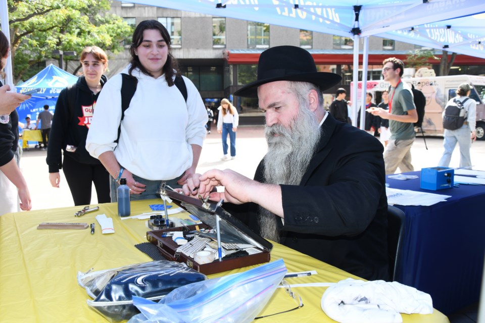 Rabbi Yehvdah Mamasheh Goldstein writes Ayala Fortinsky's name on a scoll in Hebrew.