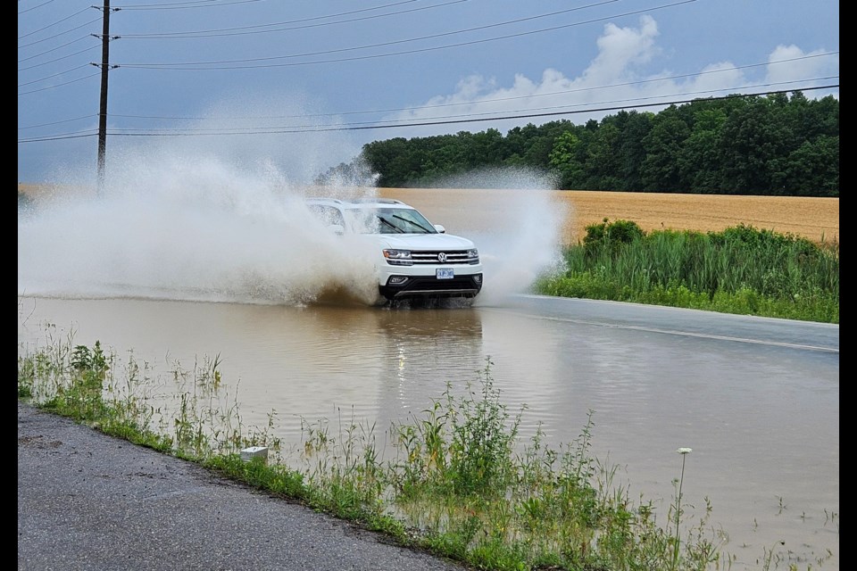 An SUV drives through the water covering 10 Sideroad between Eighth and Ninth Line.