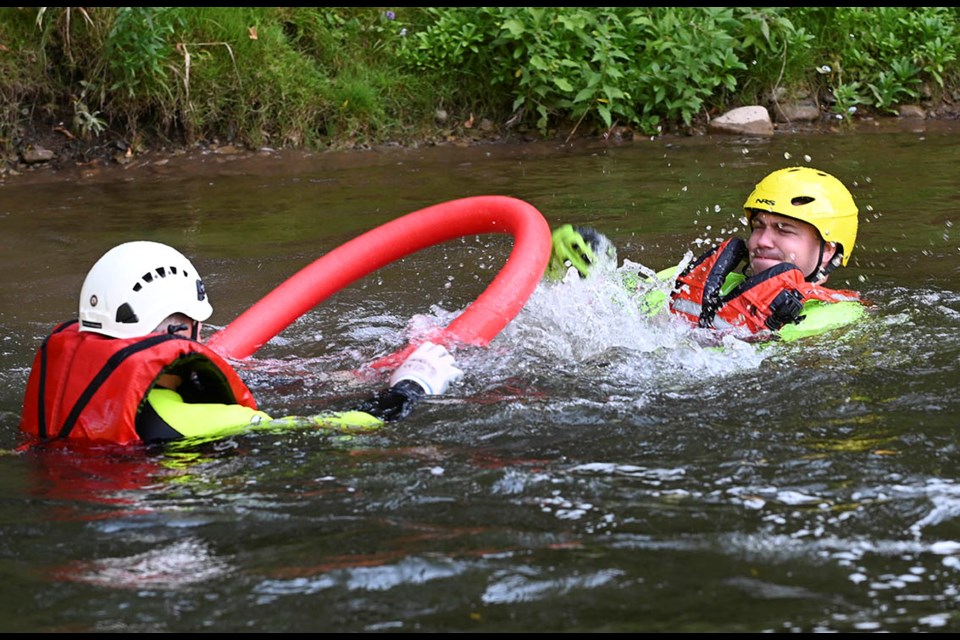 Firefighter Jeff Inglis, left, swims toward fellow firefighter/mock victim Ken Leibel with a rescue ring. The two are wearing specialized rescue wet suits during this swift water rescue training scenario.