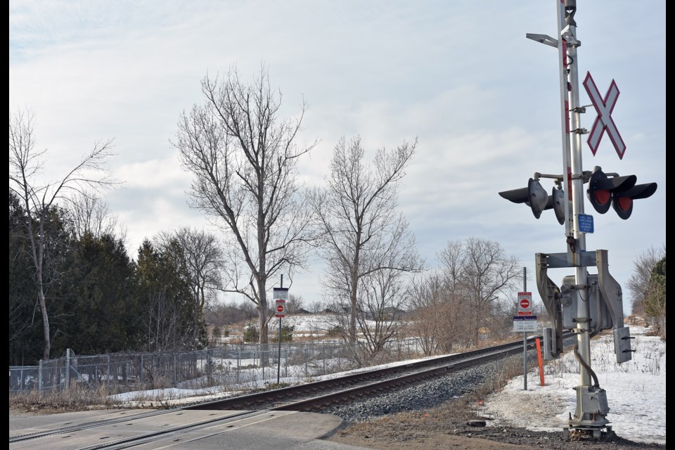 Metrolinx rail crossing in Stroud. In distance, rooftops of Innisfil Estates are just visible, over the berm.