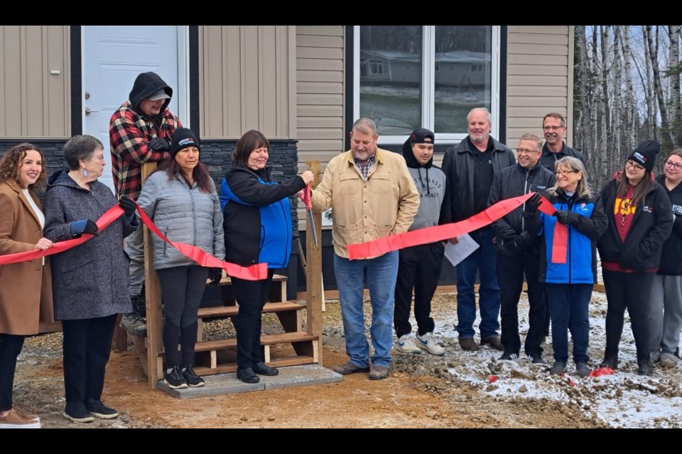 Valerie Quintal, president of Conklin Metis Local#193 who also serves as a board member for the Conklin Resource Development Advisory Committee (CRDAC), and Alex Pourbaix of Cenovus hold a large pair of scissors after cutting the ribbon celebrating the new housing development in Conklin that was made possible through grants by the provincial government and Cenovus. Photo supplied. 