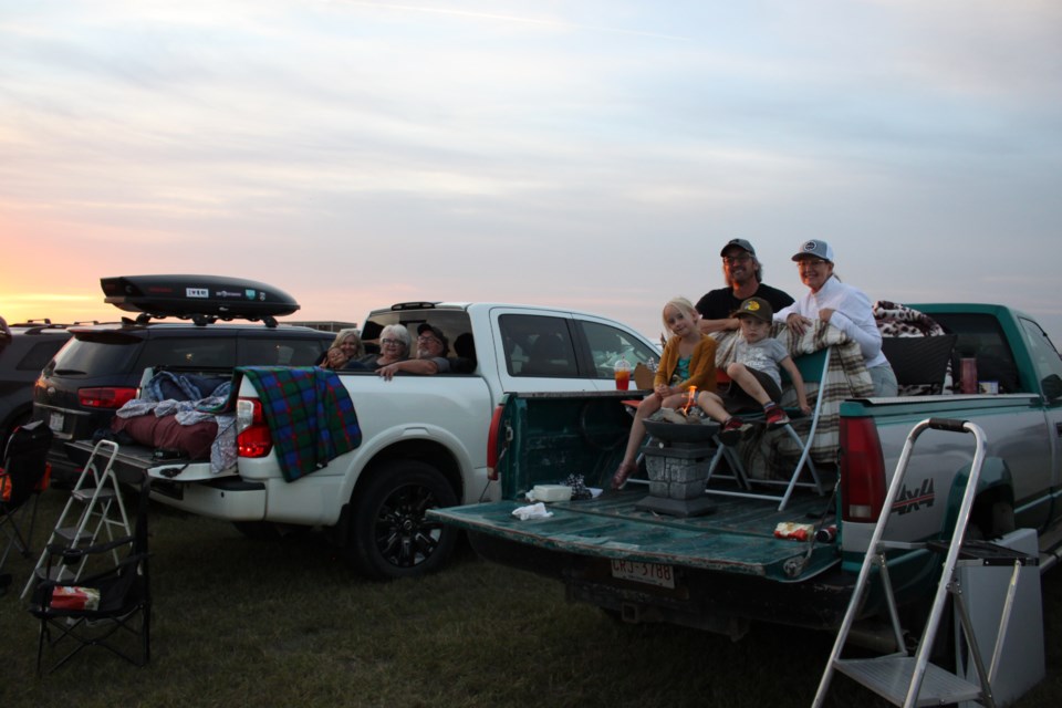 Community members came prepared to the Movie in the Park. 
from the left Natalie Kelly, Zayne Eddamni, Pat Michaud, and Leo Michaud cozy up in the far truck while Dan Chatel, Iris Scherger, Summer Scherger and Cash Scherger keep warm with their camp stove in the near truck.